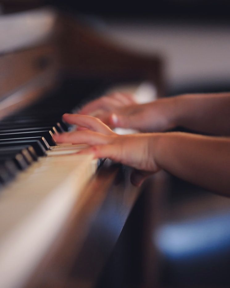 Hands playing an upright piano in warm light